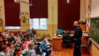 Policjant prowadzi zajęcia z dziećmi w klasie.