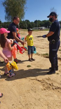 Policjant stoi na piaszczystej plaży i przekazuje prezenty dzieciom.