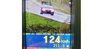 Na zdjęciu ekran wideorejestratora na którym widać samochód marki mazda i odczyt pomiaru prędkości 124 km/ h. w tle pieszy idący chodnikiem.