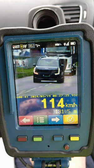 Zdjęcie ekranu ręcznego laserowego miernika prędkości z pomiarem 114 kilometrów na godzinę. Na ekranie widać sfotografowany samochód marki KIA Sportage.