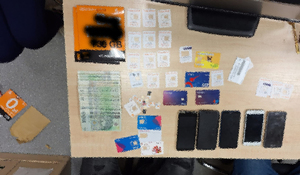 Zdjęcie stołu na którym leża rozłożone przedmioty zabezpieczone przy oszustach. 5 smartfonów, liczne karty prepaydowe i gotówka.
